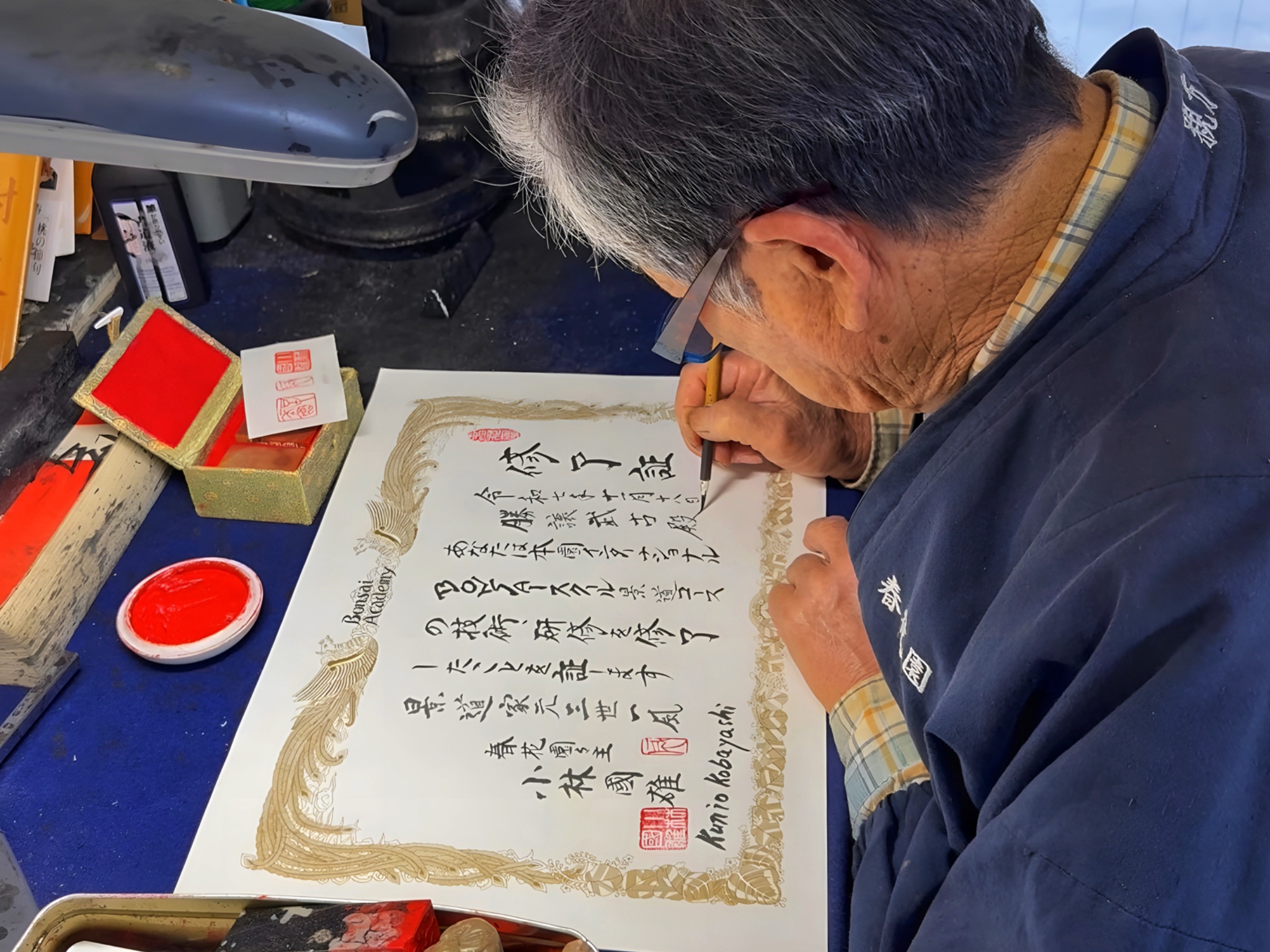 Kobayashi Ippū caligrafiando a mano con pincel y tinta el diploma de finalización N.º&nbsp;1 de Marcial Yuste Blasco, con más de 60 kanji y cuatro hanko